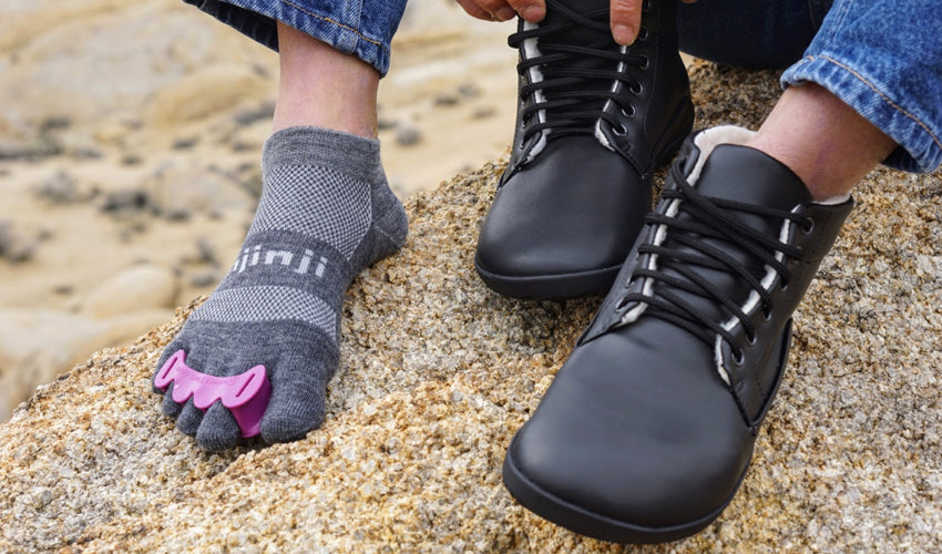 A seated hiker sporting a combination of Correct Toes Plum toe spacers, Injinji toe socks, and Ahinsa Bare Ankle Lifo+ boots