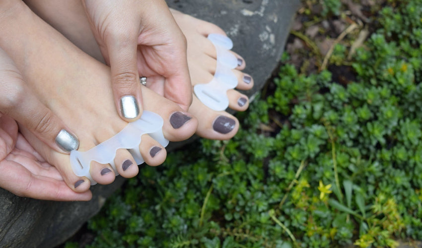 A person applying Correct Toes Original toe spacers on bare toes in a garden setting