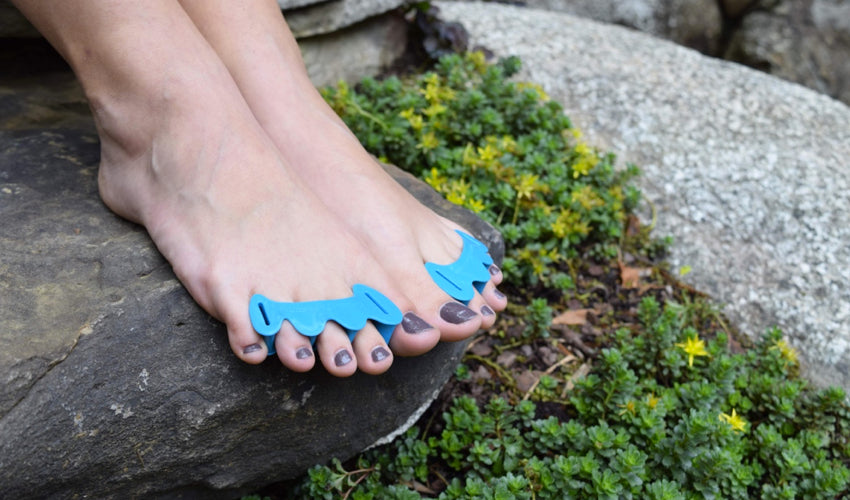 Correct Toes Aqua-Zehenspreizer an den Füßen einer Person, die auf einem Stein in einem Garten sitzt