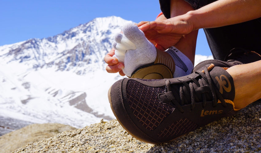 A hiker in Lems Primal 2 Brown shoes putting on a pair of Correct Toes toe spacers