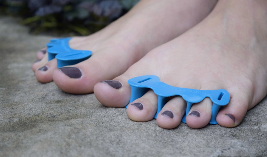 A close-up image of Correct Toes Aqua toe spacers on bare toes in a garden setting