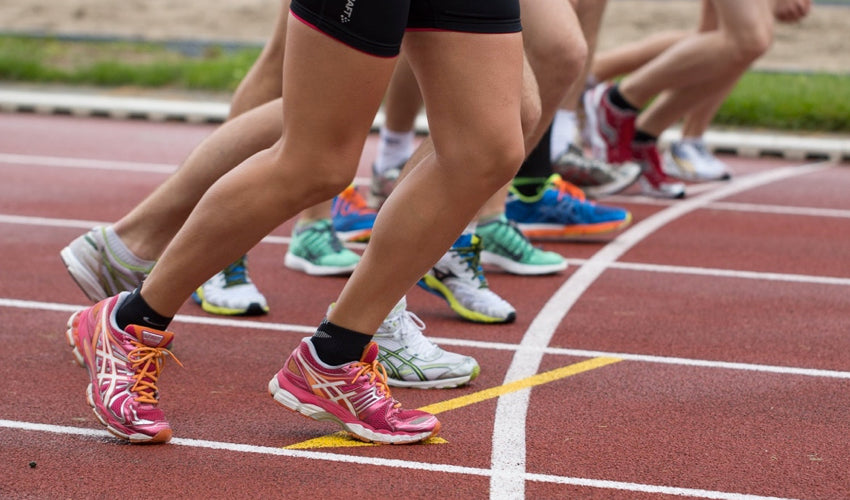 A row of runners, all wearing conventional running shoes, lined up at the starting line of a track race