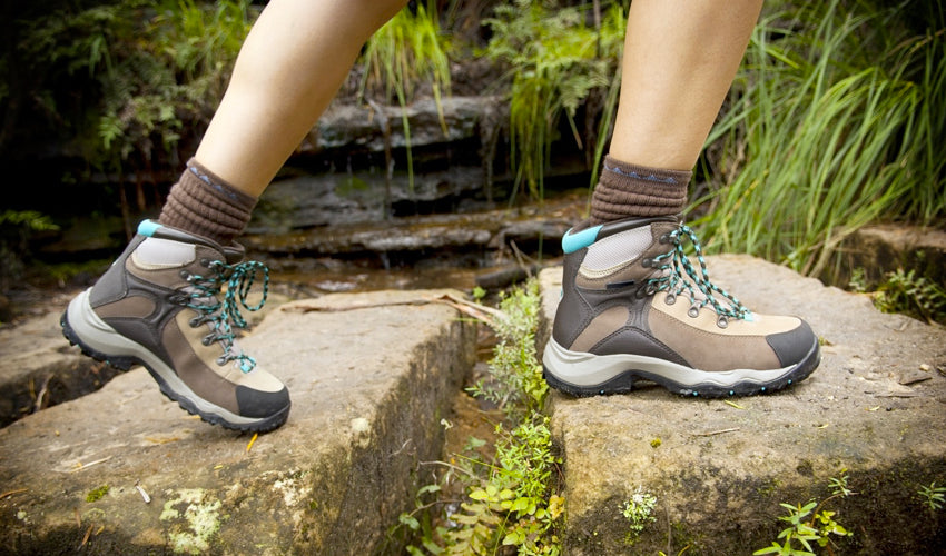 A hiker wearing thick-soled hiking boots and stepping from one stone to the next