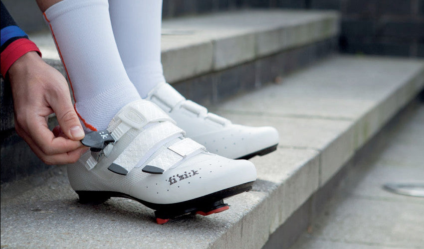 A cyclist, seated on concrete steps, securing the strap of a conventional cycling shoe