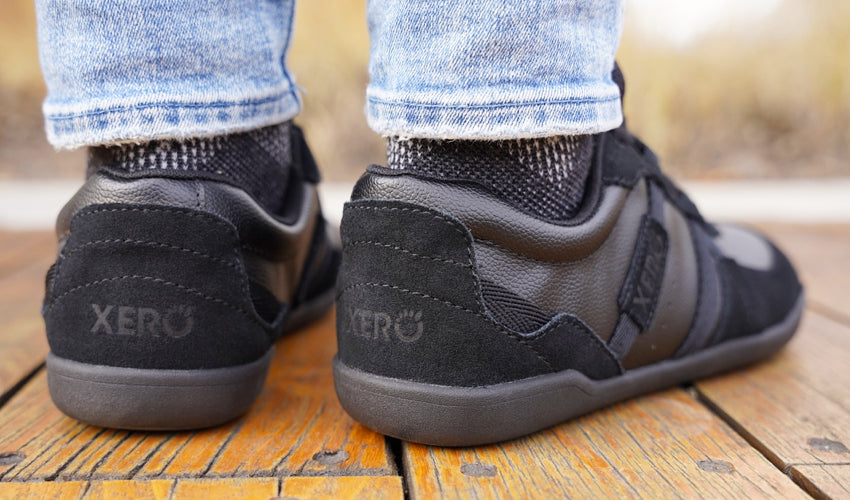 Rear-diagonal view of the feet of a person wearing Xero Kelso Black shoes