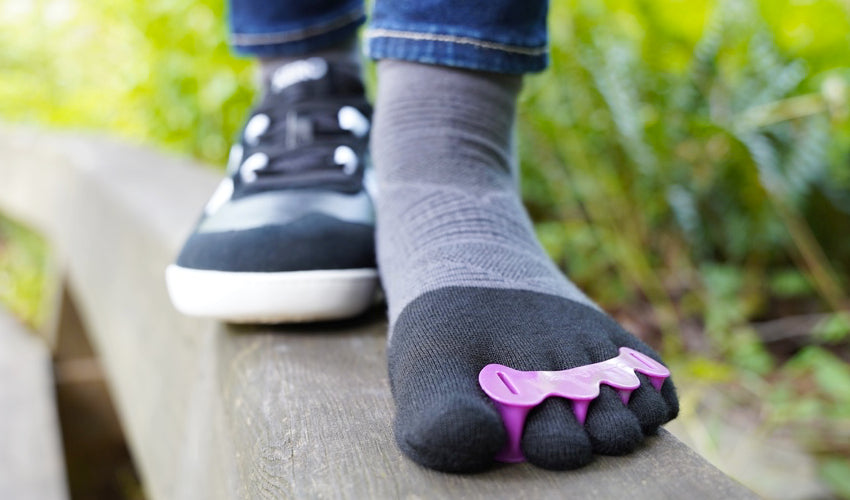 Frontal view of the feet of a person wearing a Xero Kelso shoe on one foot and an Injinji toe sock and Correct Toes toe spacer on the other foot