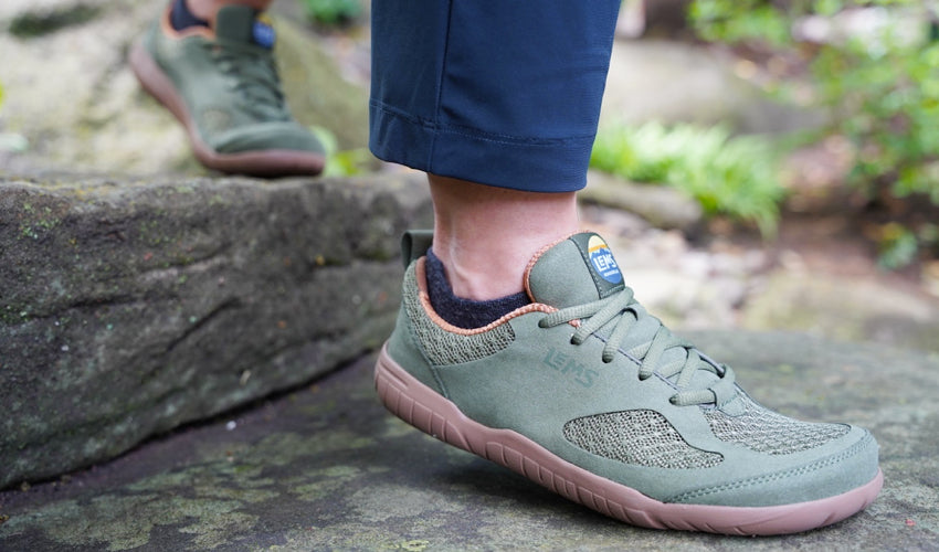 A person wearing Lems Primal 3 Olive shoes descending a stone staircase in a garden setting