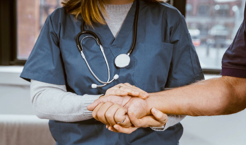 A female physician with a stethoscope around her neck holding the hand of her patient