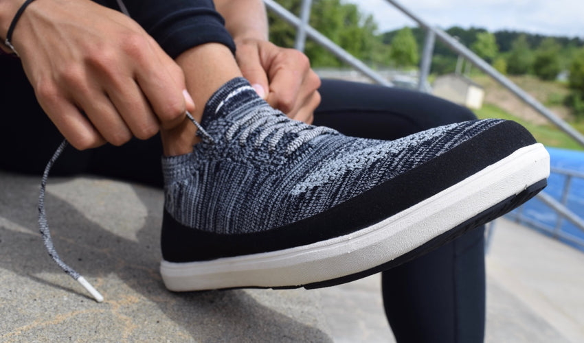 A person, sitting on a concrete step, lacing up a pair of Altra Vali shoes