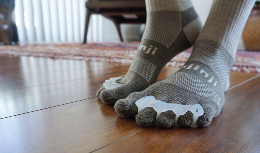 A person wearing Correct Toes and Injinji toe socks on hardwood floors