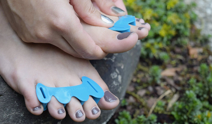A close-up view of a person in a garden setting putting on a pair of Correct Toes Aqua toe spacers