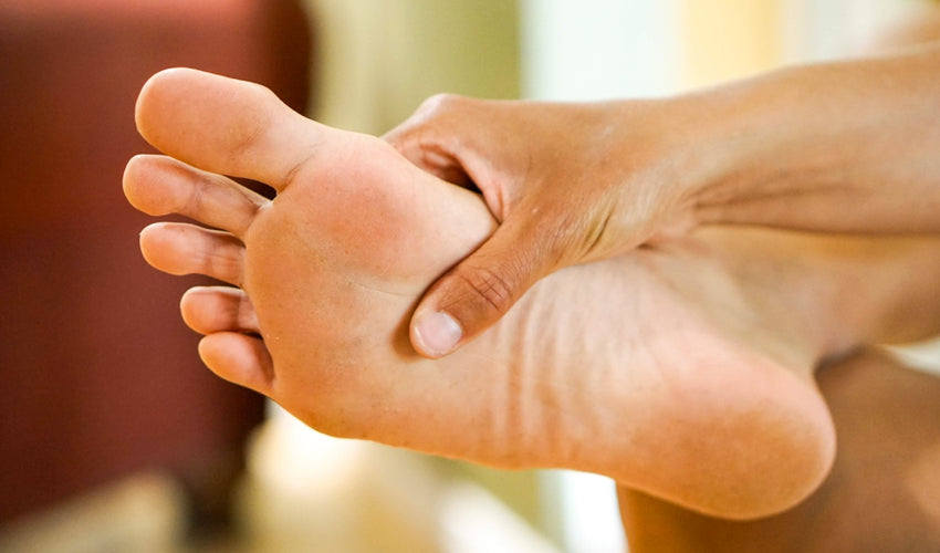 A person pressing their thumb into the sole of their foot, just behind the ball of their foot