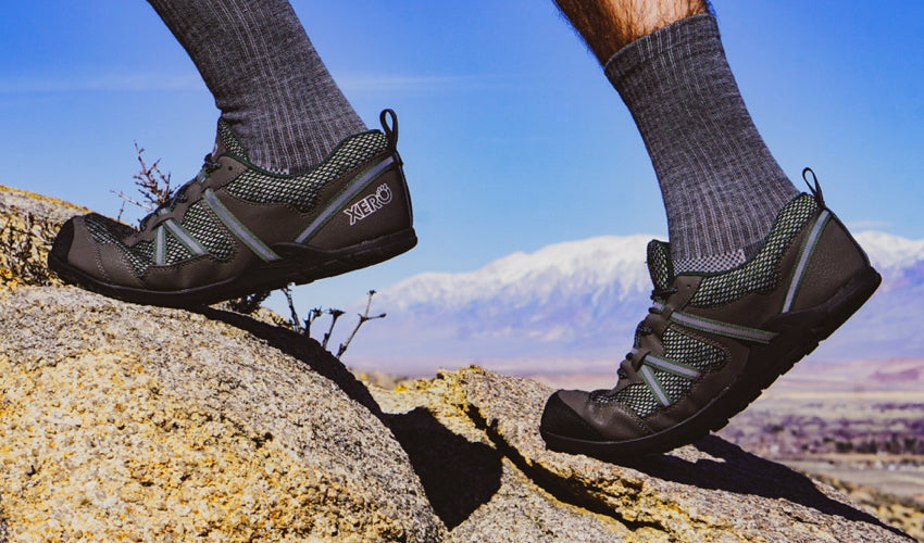 A side view of Xero TerraFlex athletic shoes worn by a trail runner with mountains in the background