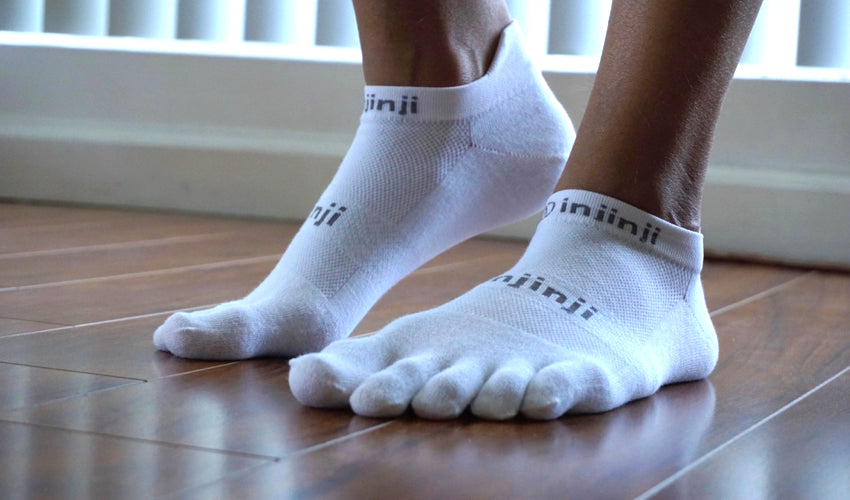 A person wearing Injinji No Show toe socks in White on a hardwood floor