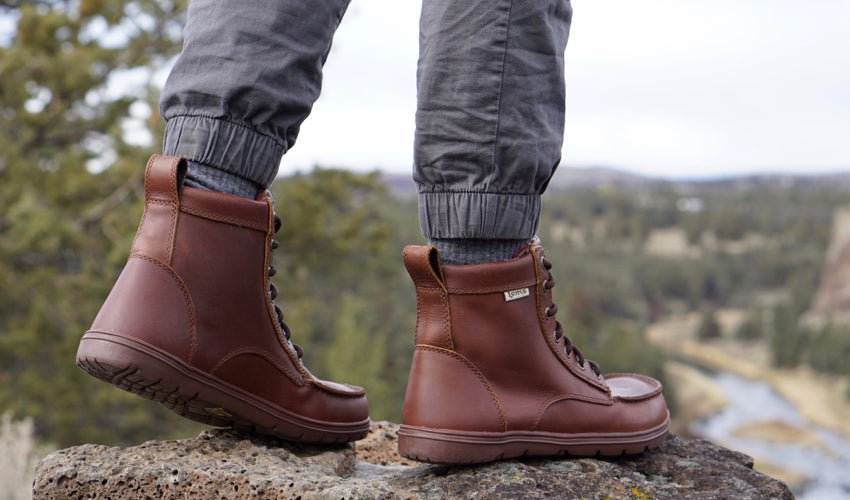 A hiker wearing Lems Boulder Boots in Leather Russet with a river and valley in the background