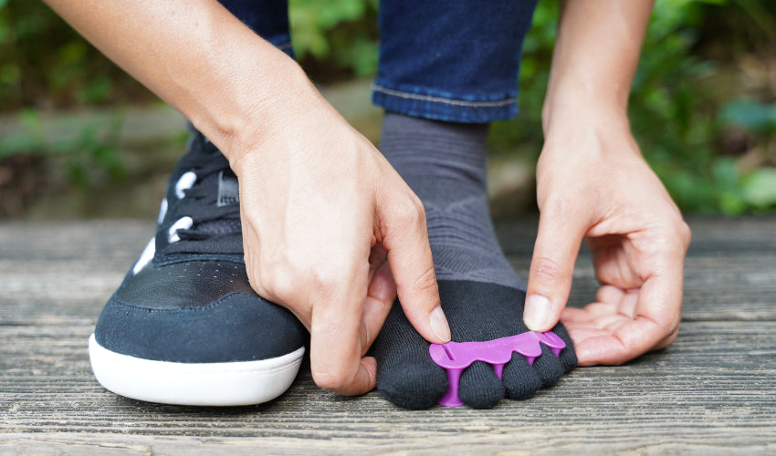 Front view of a person seated on a wooden bench wearing Xero Kelso shoes and putting on a Correct Toes Original toe spacer