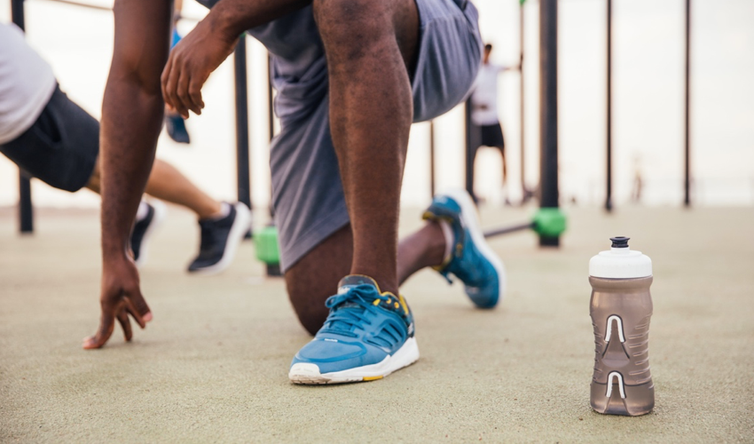 Male athlete in conventional athletic shoes kneeling on one knee, stretching his hip flexors