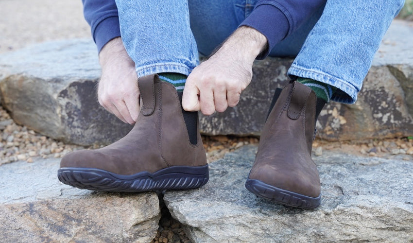 Person seated on a stone step and donning a Lems Chelsea Boot Waterproof Espresso boot