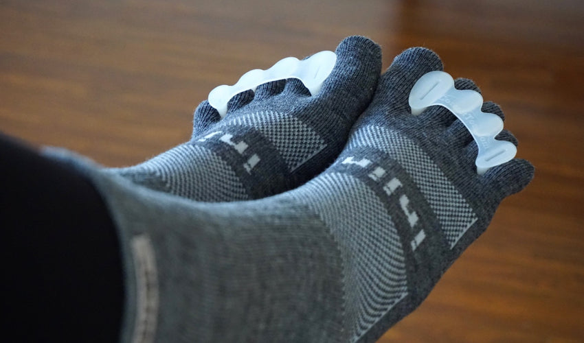 A set of feet wearing Injinji toe socks and Correct Toes toe spacers