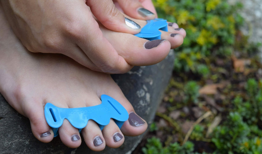 A person donning a pair of Correct Toes Aqua toe spacers in a garden setting