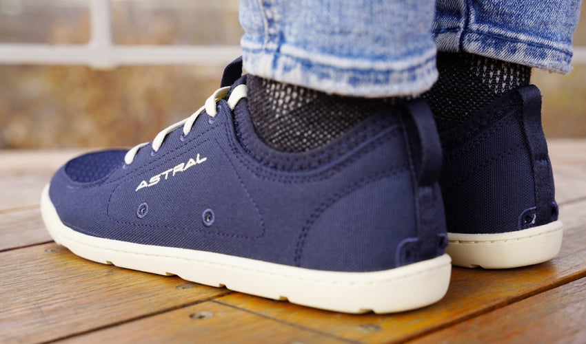 A rear-diagonal view of a set of feet wearing Astral Loyak shoes in Navy/White