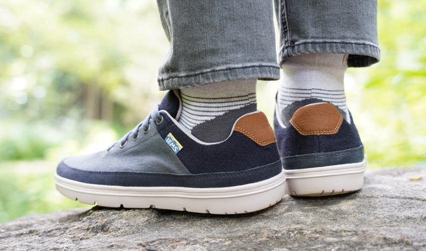 Diagonal/rear view of a pair of Lems Chillum Varsity Blue shoes worn by a person standing on a rock in nature
