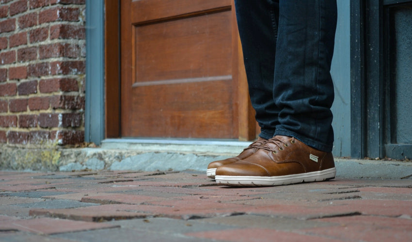 A person on a brick cobblestone street wearing Lems Nine2five dress shoes in Coffee & Cream