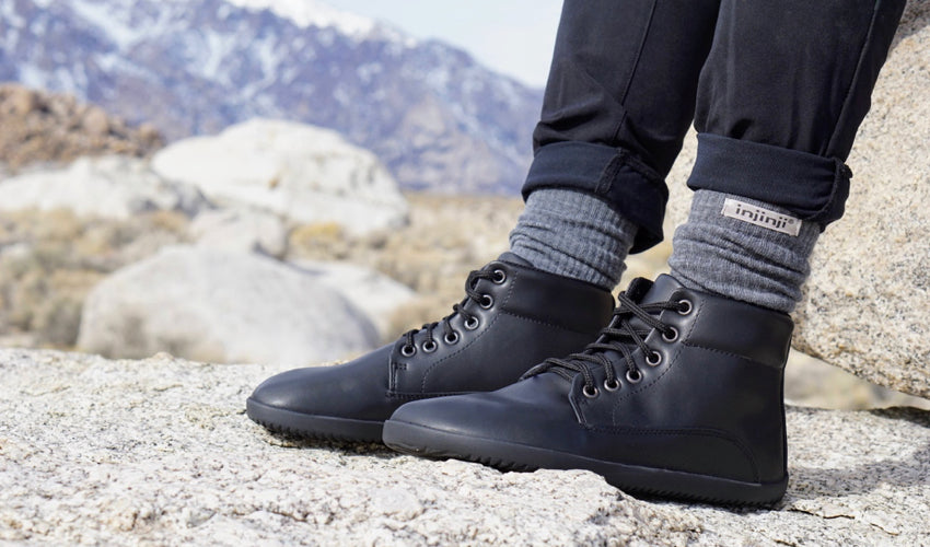 Person wearing Ahinsa Sundara Ankle Barefoot boots and Injinji toe socks with mountains and large rocks in the background