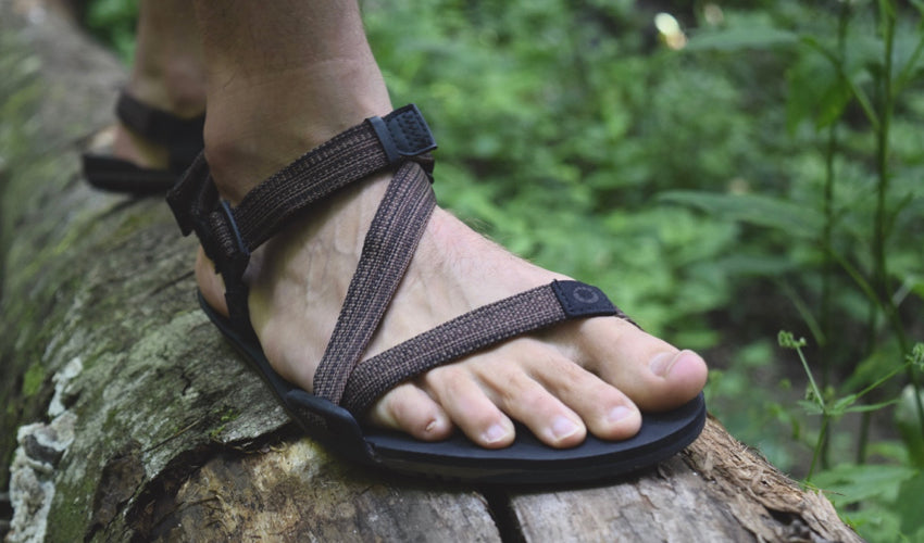 Man wearing Xero Z-Trail sports sandals and standing on a log in the forest