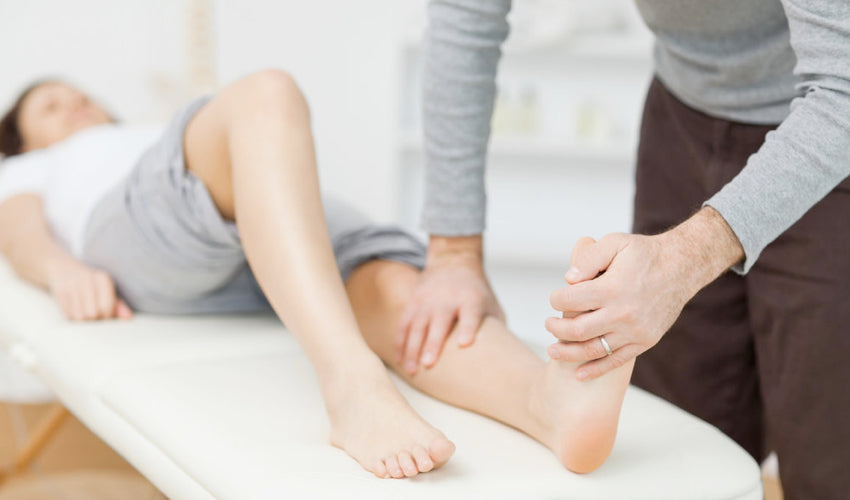 A healthcare provider stretching the bottom of a supine patient's left foot