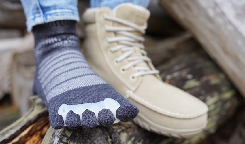 Diagonal view of a set of feet with one foot wearing a Lems Telluride Boot and the other a Correct Toes toe spacer over an Injinji toe sock