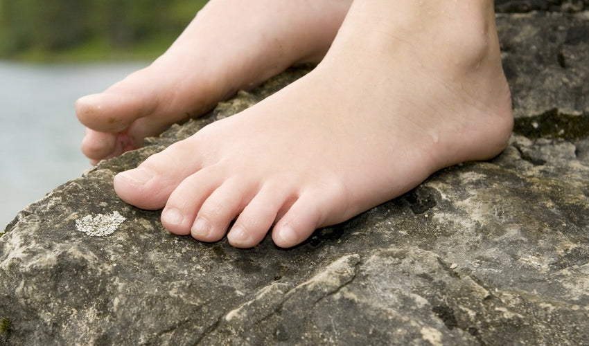 A pair of bare feet resting on a rock with a lake in the background