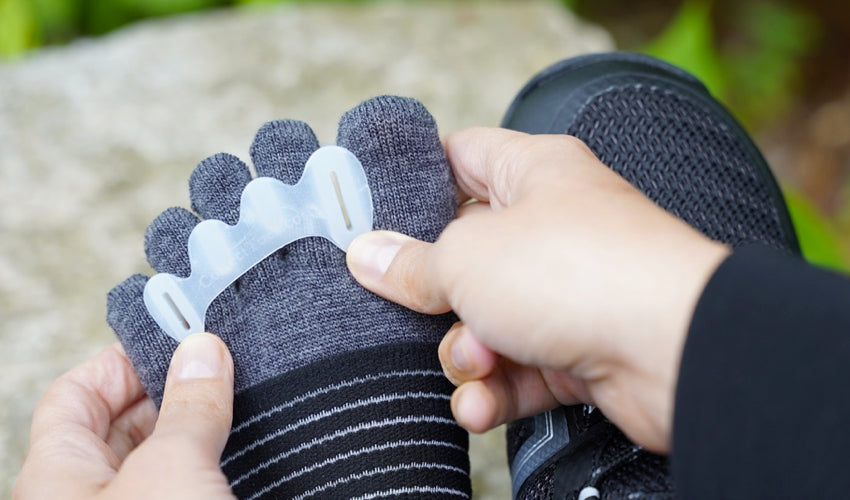 A Xero Xcursion Fusion boot wearer applying a Correct Toes toe spacer over an Injinji toe sock