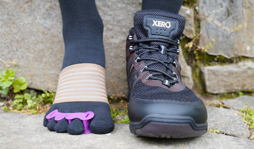 Face-on image of a Xero Xcursion Fusion boot wearer with one foot exposed and wearing a Correct Toes toe spacer and an Injinji toe sock