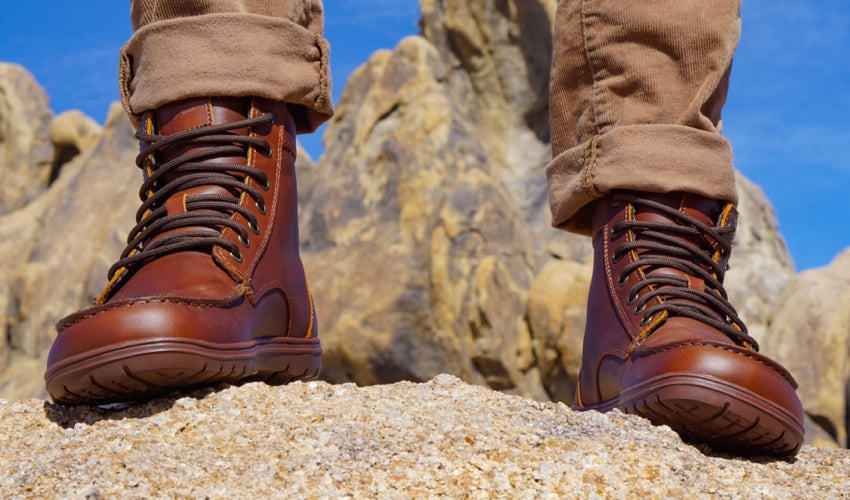 A person posing in a pair of Lems Boulder Boots in Leather Russet with blue skies and interesting rock formations in the background