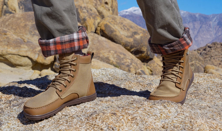 Hiker striding over rocks wearing a pair of Lems Boulder Boots in Brown