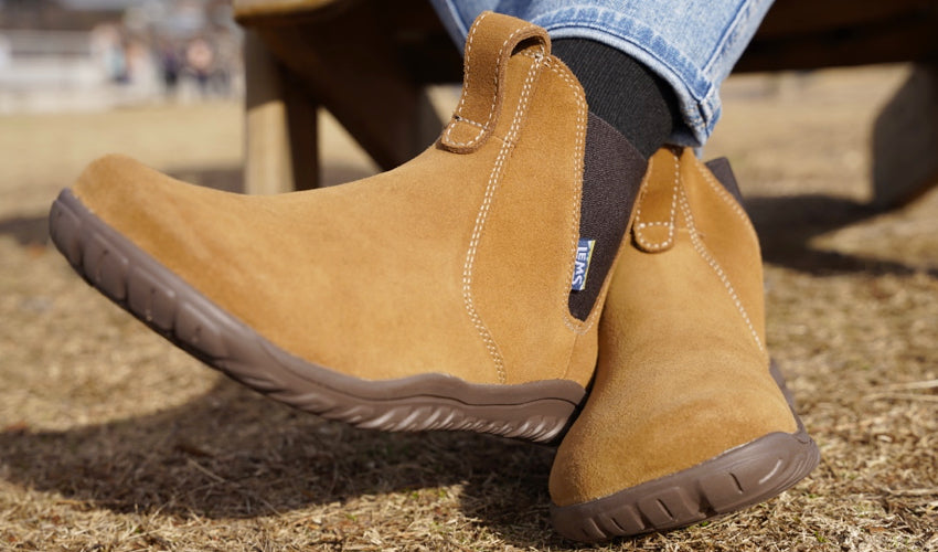 The crossed feet of a seated person wearing Lems Chelsea Boot Cedar boots