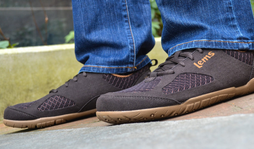 A person standing on a concrete step and wearing Lems Primal 2 Brown shoes