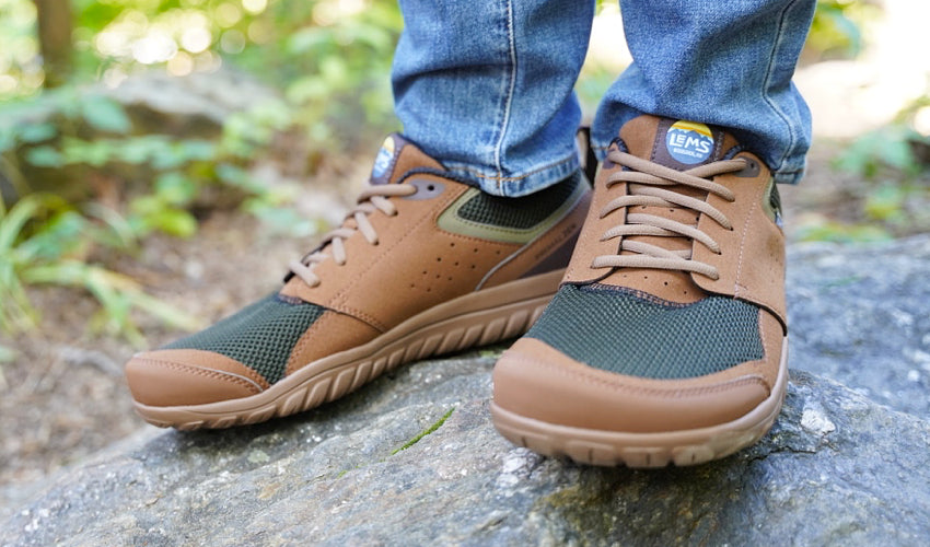 Person in the forest wearing Lems Primal Zen Woodland shoes and standing on a rock