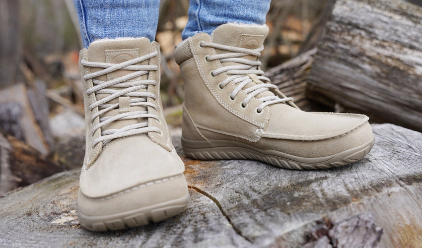 The feet of a person wearing Lems Telluride Boots standing on a well-aged block of wood