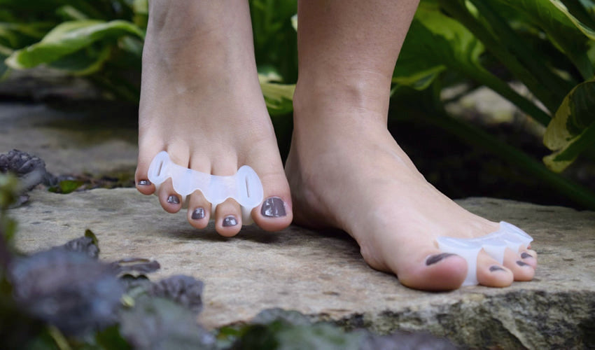 A barefooted person in a garden setting wearing Correct Toes Original toe spacers