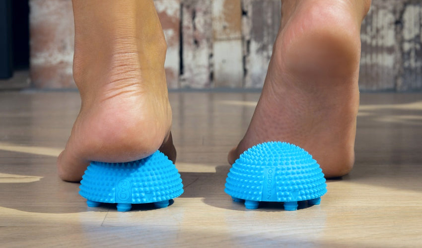 Person standing on two separated halves of a Naboso Neuro Ball and performing a therapeutic foot exercise