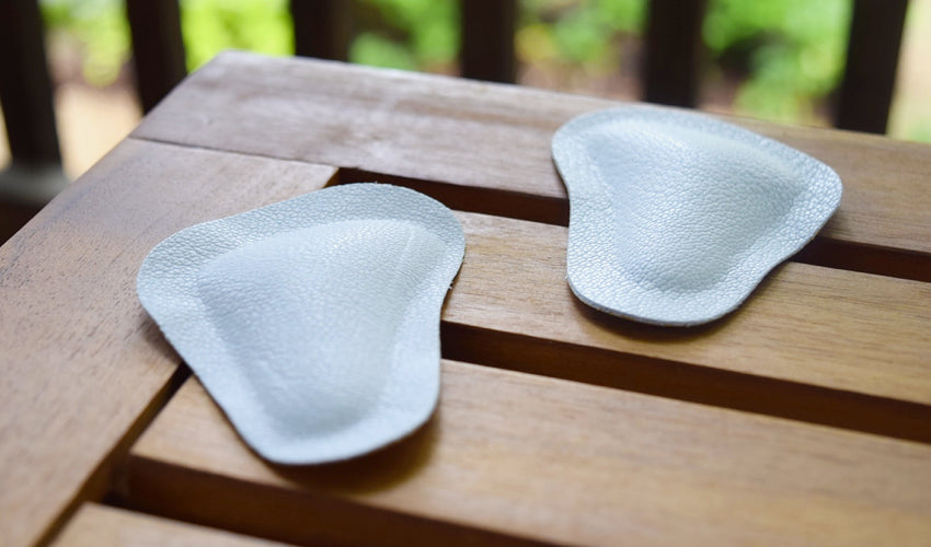A pair of Pedag metatarsal pads on a slatted wooden table.