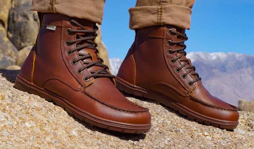 Hiker wearing Lems Boulder Boots in Leather Russet with snow-capped peaks in the background