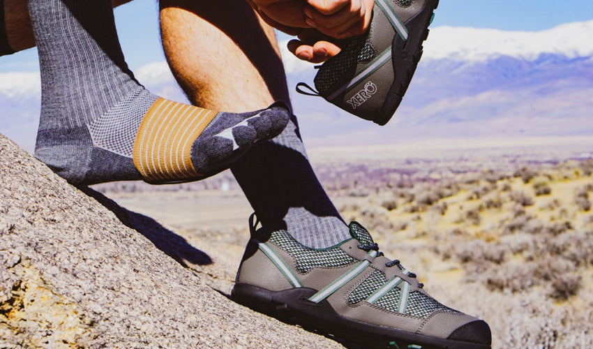 A hiker putting on Xero TerraFlex trail shoes, Correct Toes toe spacers, Strutz foot pads, and Injinji toe socks