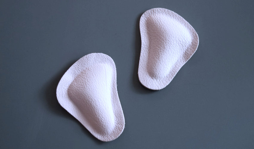 A top-down view of a pair of Pedag metatarsal pads sitting on a blue desk