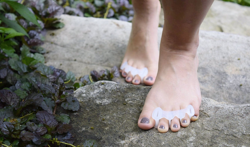 A barefooted person wearing Correct Toes and climbing a set of stone steps in a garden setting