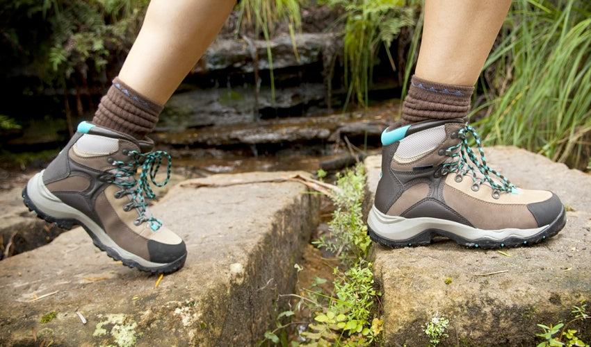 Female hiker wearing conventional hiking boots and walking over cut stones near a river