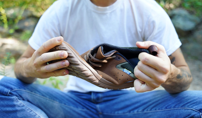 Seated person twisting a Lems Primal Zen Woodland shoe to show the degree of sole flexibility it possesses