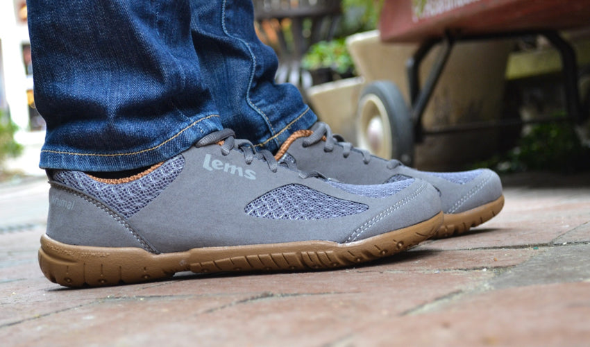 Close up view of a pair of Lems Primal 2 Slate shoes with cobblestones in the foreground